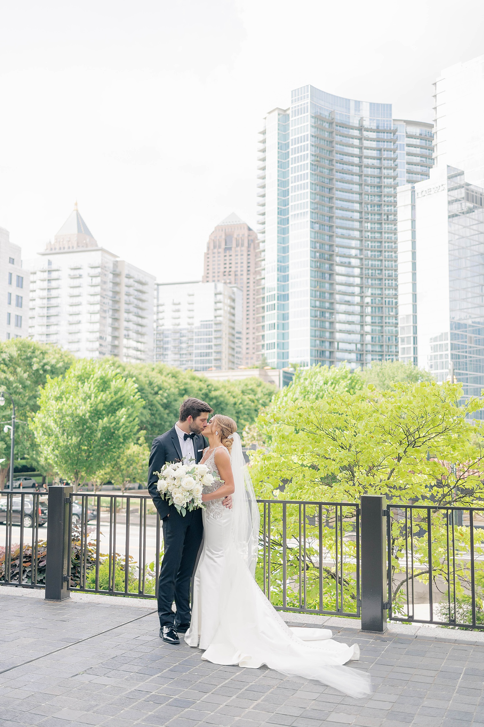 bride and groom kiss with the Atlanta skyline in the background outside Peachtree Club wedding venue