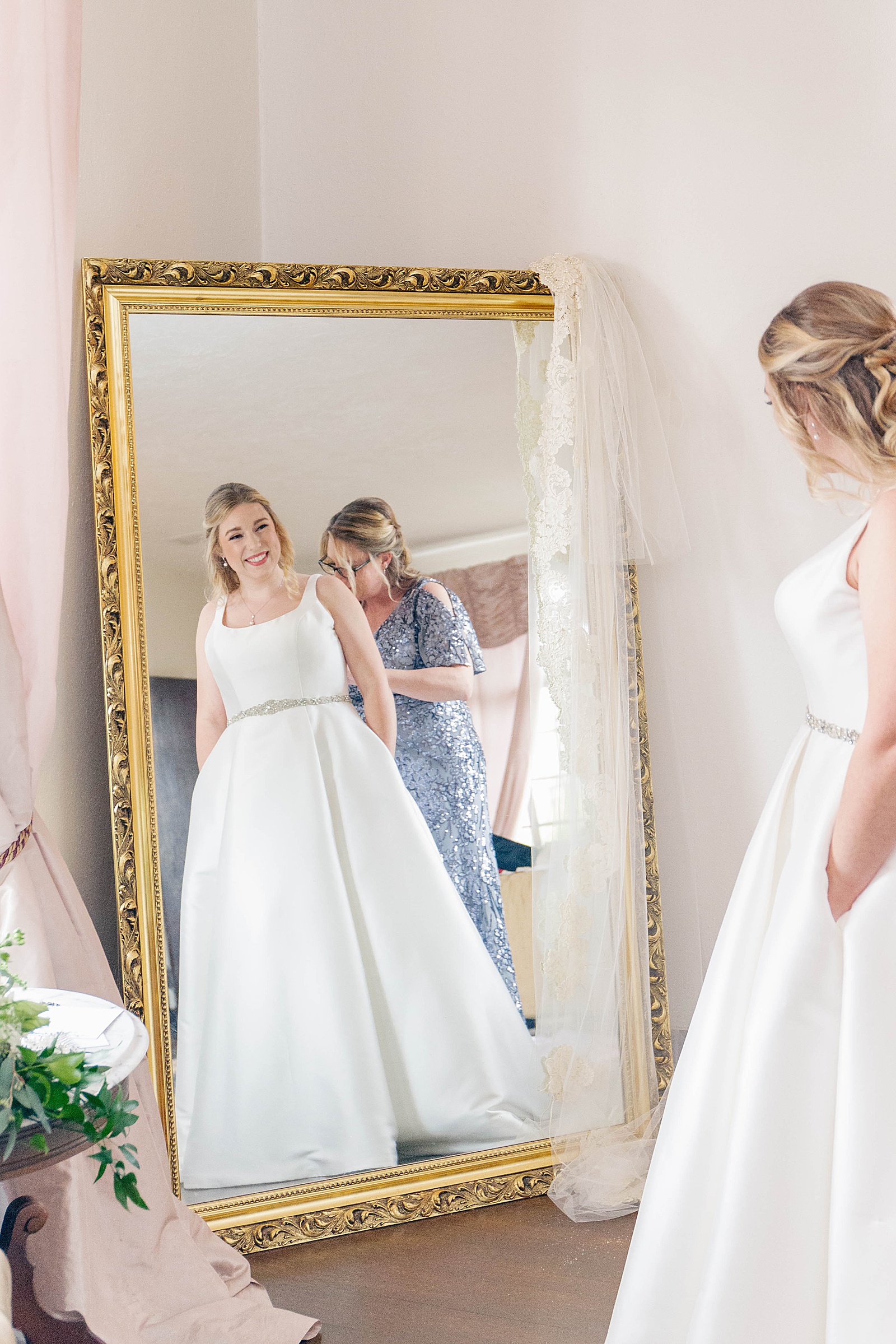 bride in wedding gown from Atlanta GA wedding dress shop looking at herself in a gold mirror before wedding ceremony.
