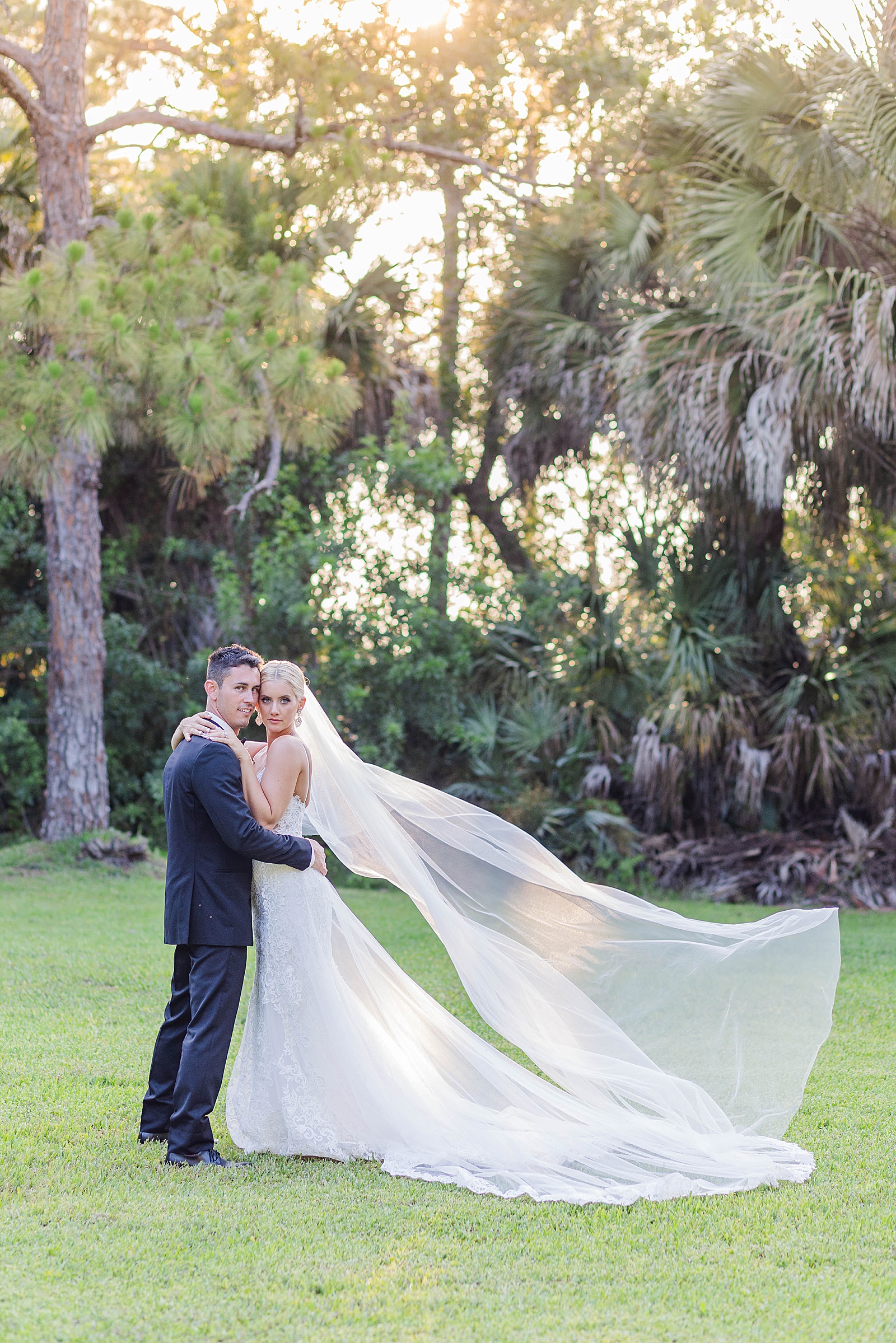bride and groom pose for a photo and bride's veil flowing in the wind