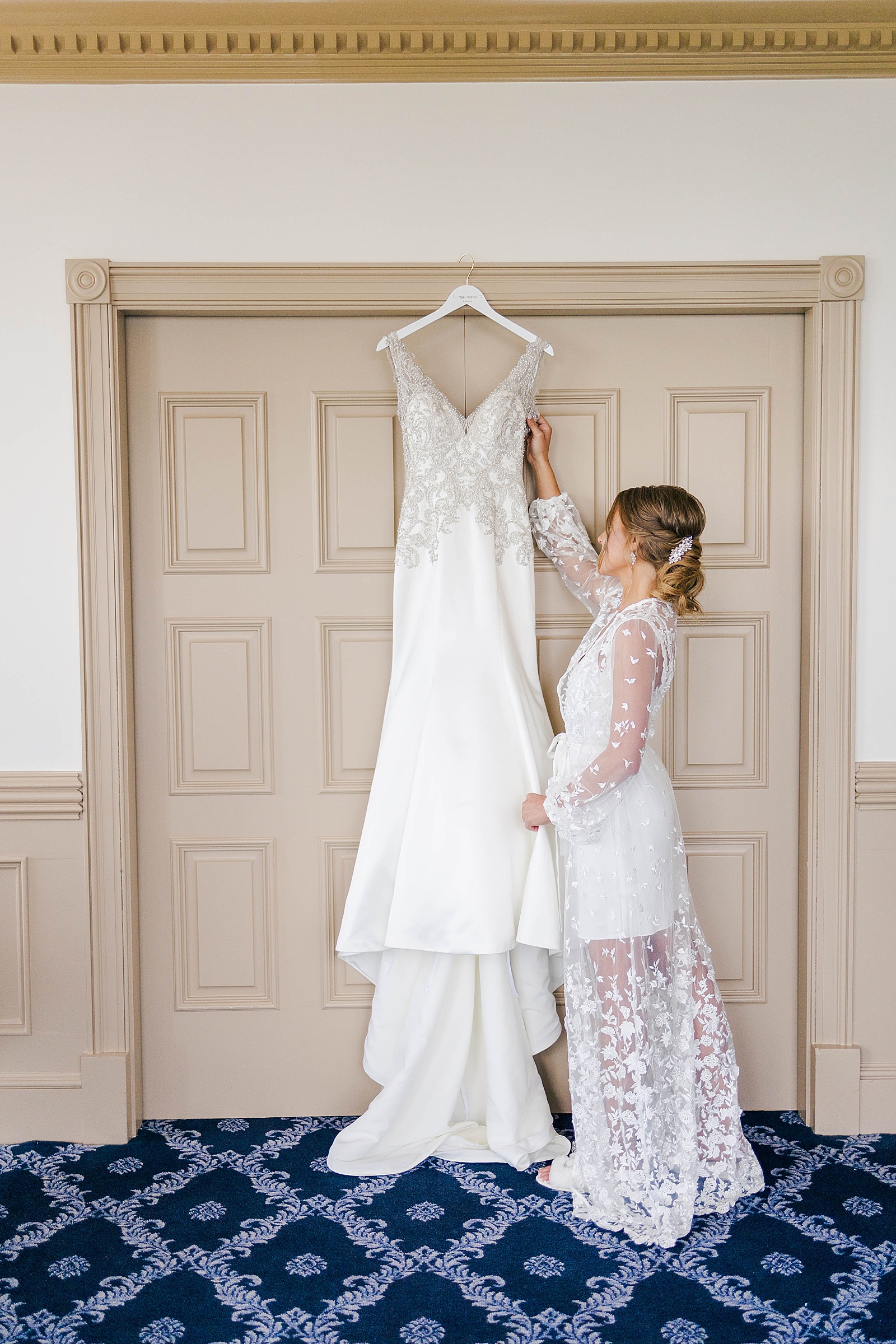 bride reaching for her white wedding dress with intricate beading from Atlanta Georgia wedding dress store hanging on a door 