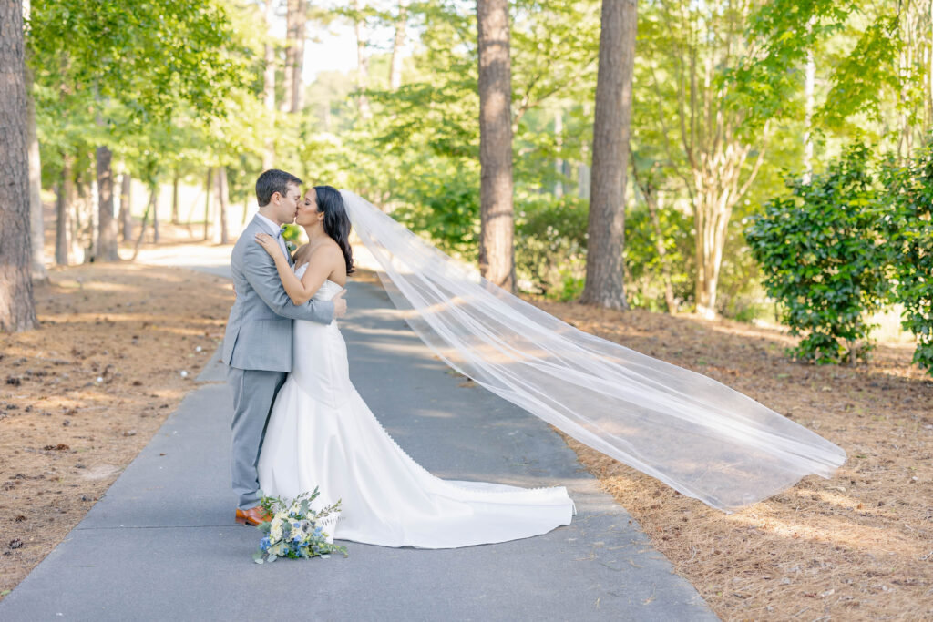 bride and groom kissing with veil in the wind posing in golf course trail at Courtry Club of the South wedding venue