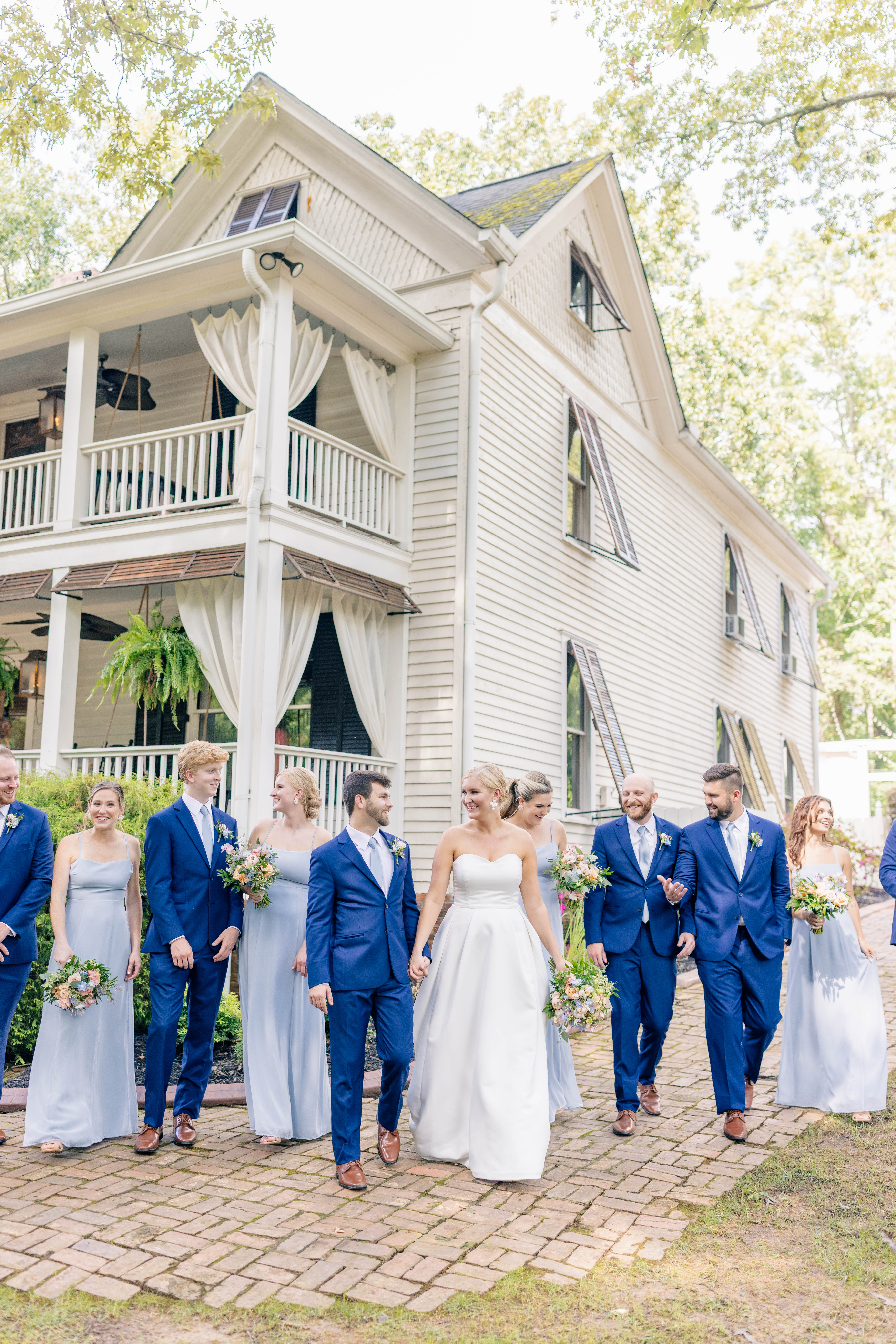 bridesmaids and groomsmen walk in front of the wheeler house wedding venue with bride and groom
