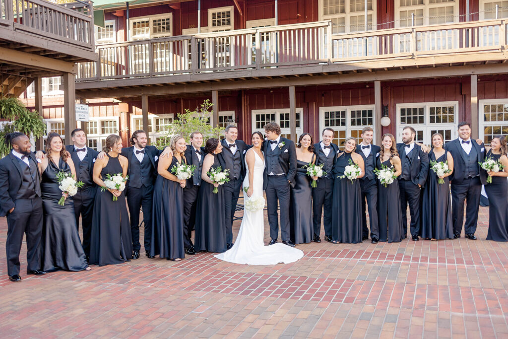 A bride and groom stand with arms around each other with their large wedding party at the Ivy Hall Wedding Venue