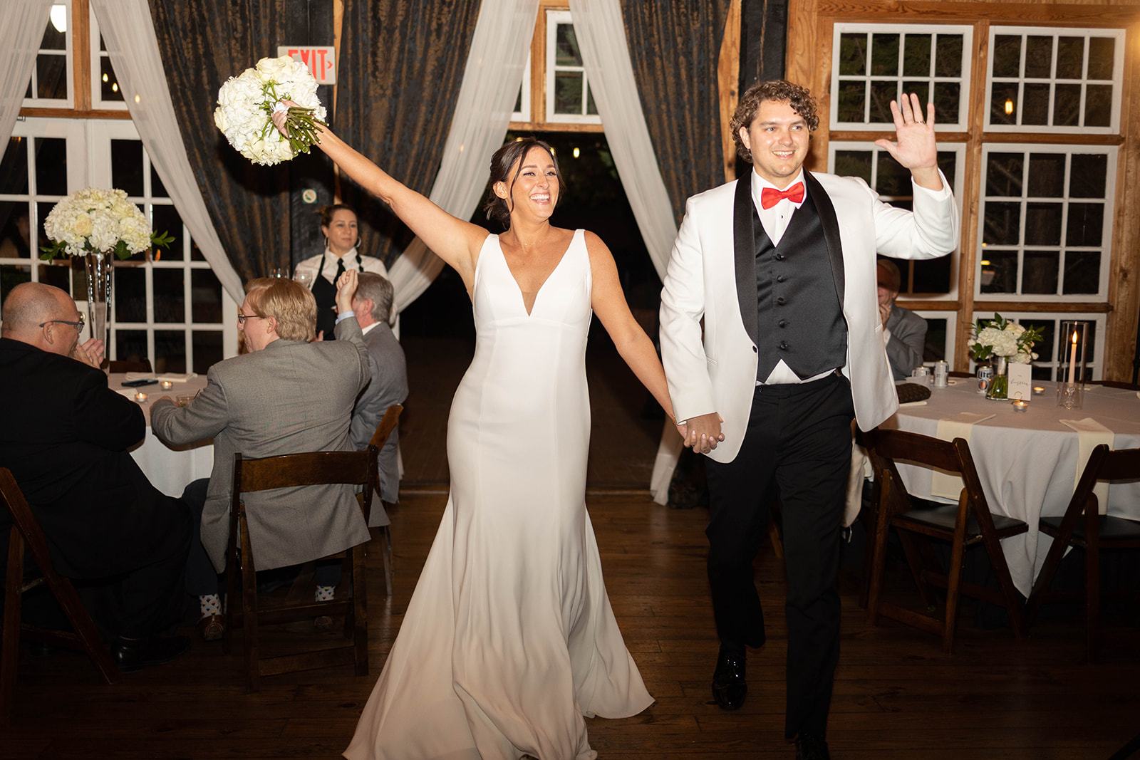 A bride and groom celebrate and wave while entering their reception