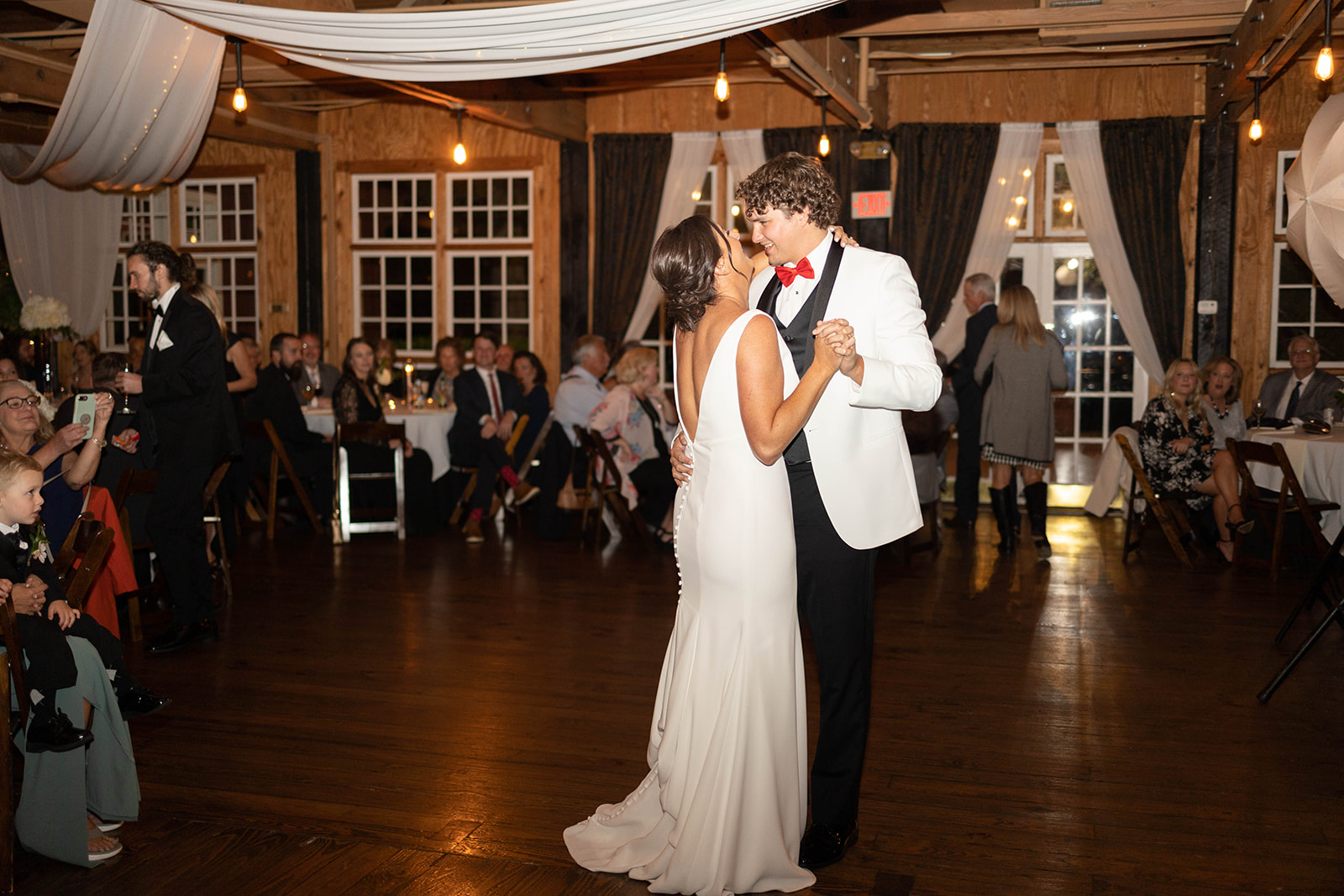 Newlyweds dance in a white jacket and silk dress on the dance floor