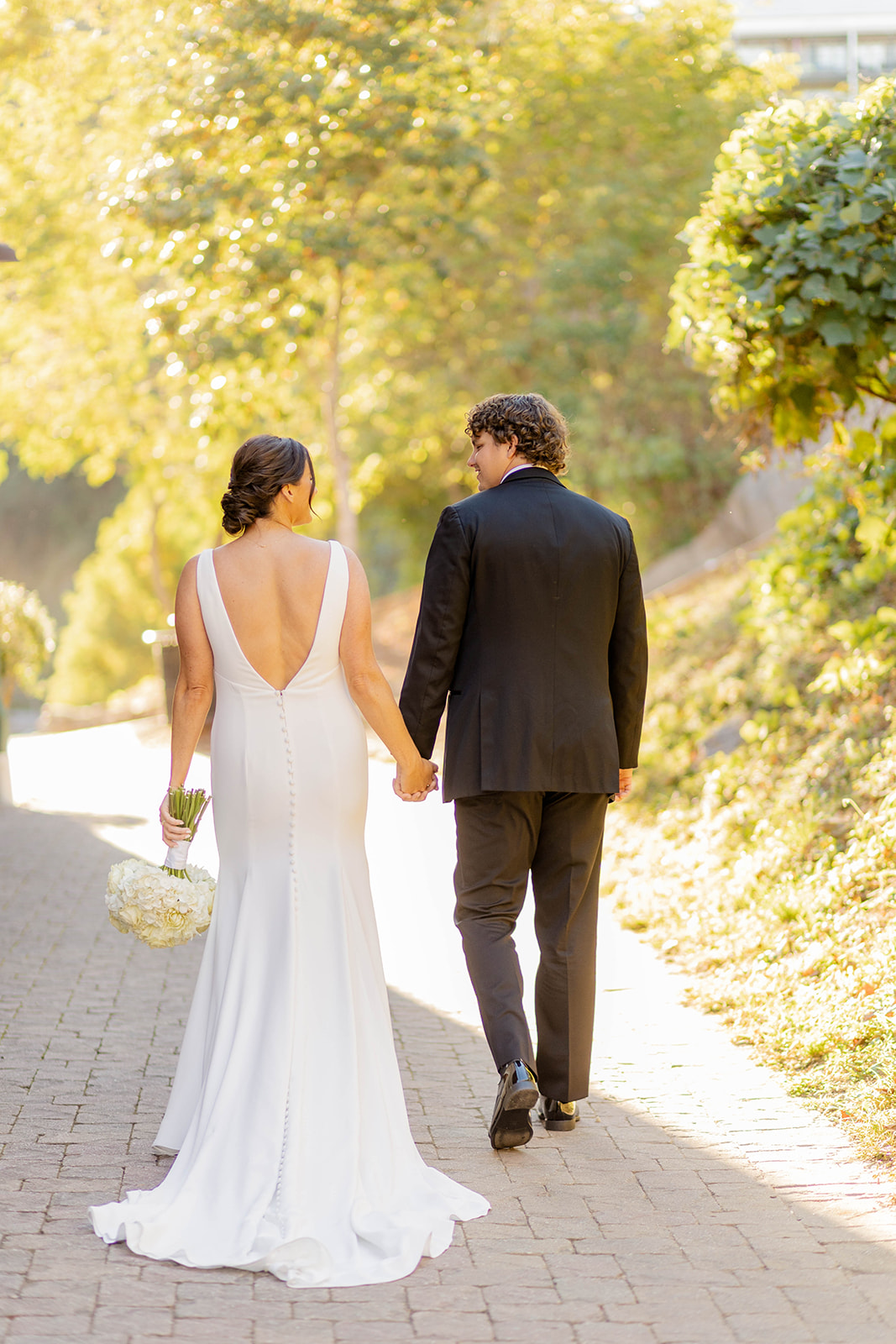Newlyweds hold hands and walk on a brick sidewalk at the Ivy Hall Wedding Venue