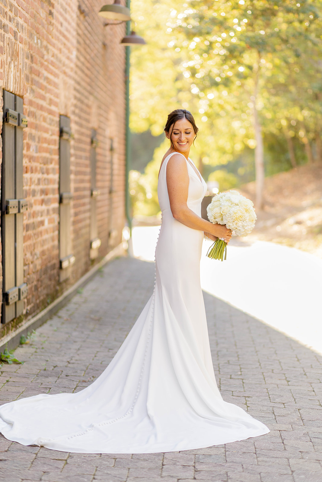 A happy bride in a silk gown smiles down her shoulder with a white bouquet at the Ivy Hall Wedding Venue