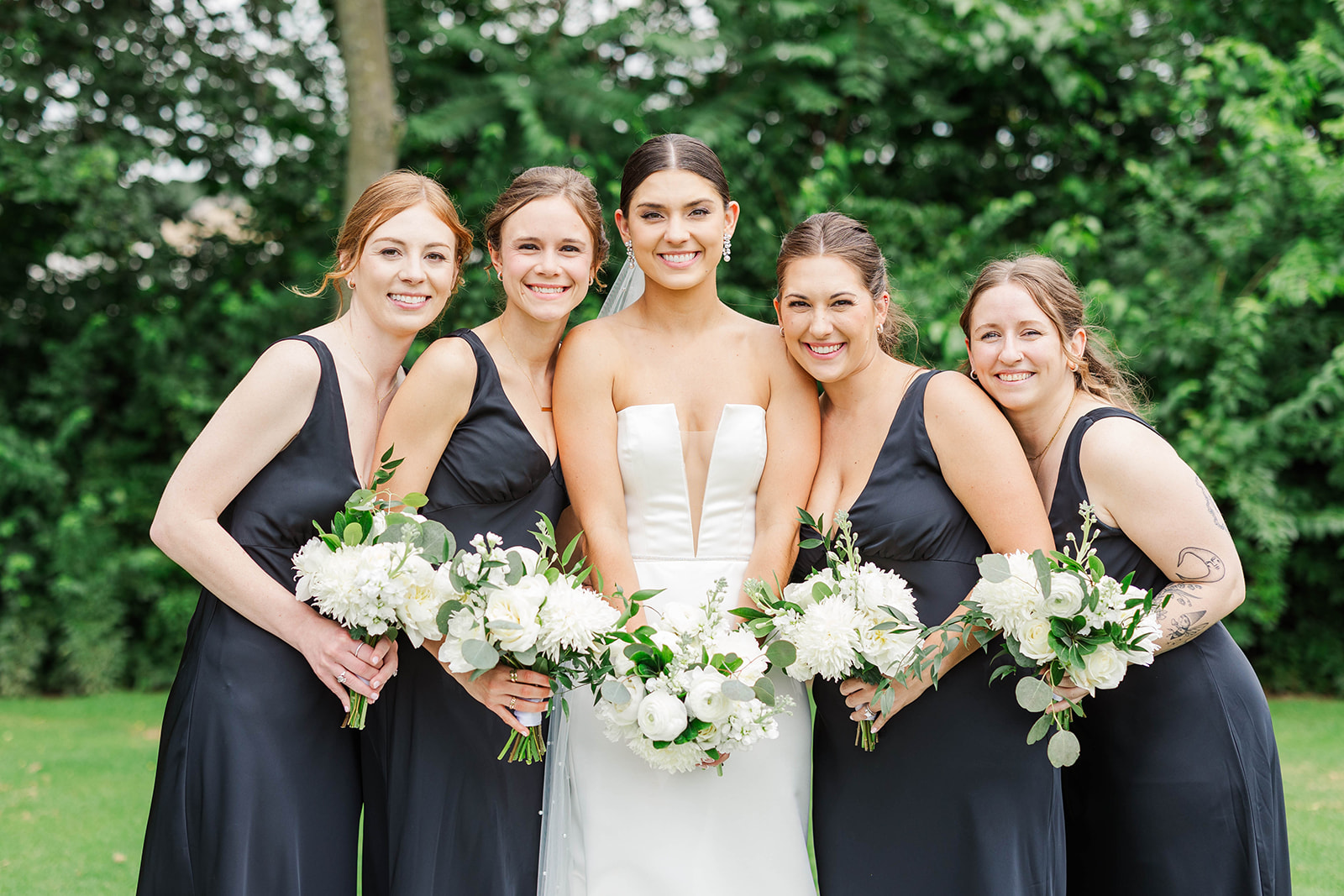 A bride smiles big with her bridesmaids in black dresses