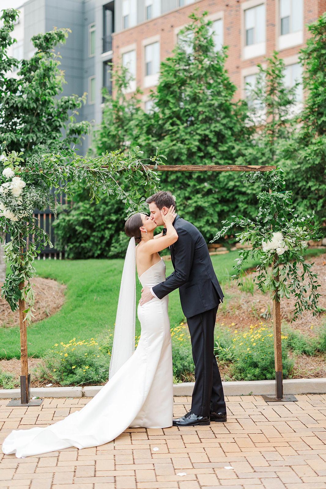A bride and groom kiss while holding each other under the wooden arbor at their Upstairs Atlanta Wedding