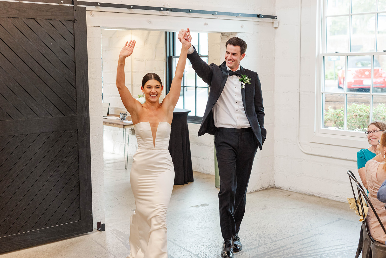 A bride and groom laugh and lift their hands while entering their cermeony