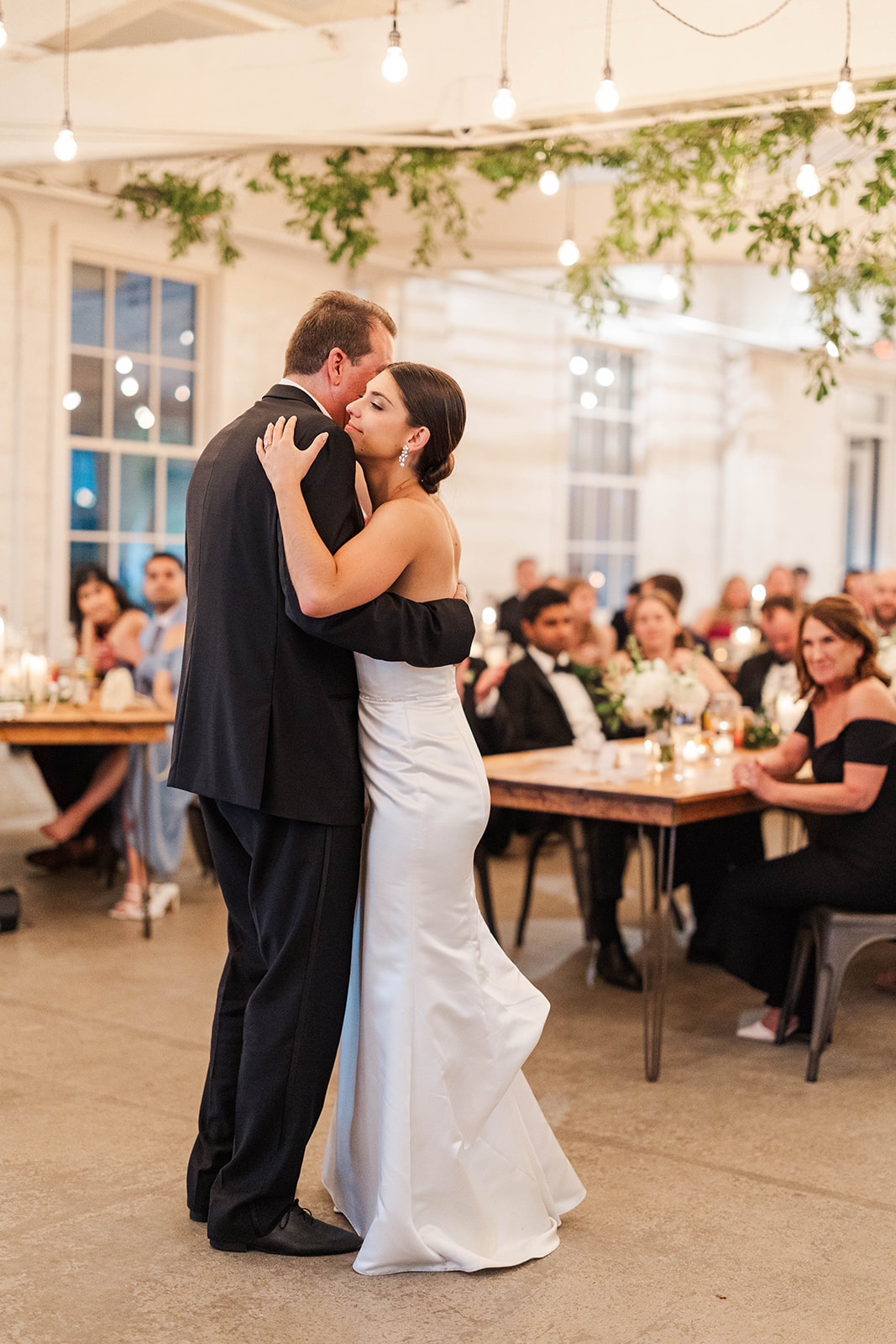 A bride dances with dad on the dance floor as guests watch