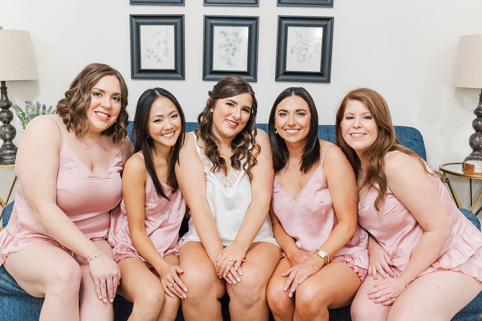 A bride sits on a bed with her bridesmaids in pink and white pajamas