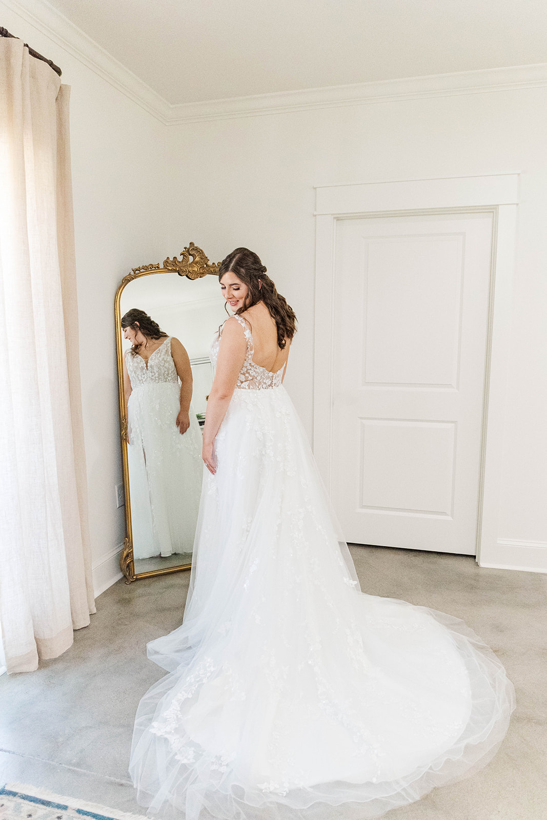A happy bride admires her dress in an antique mirror