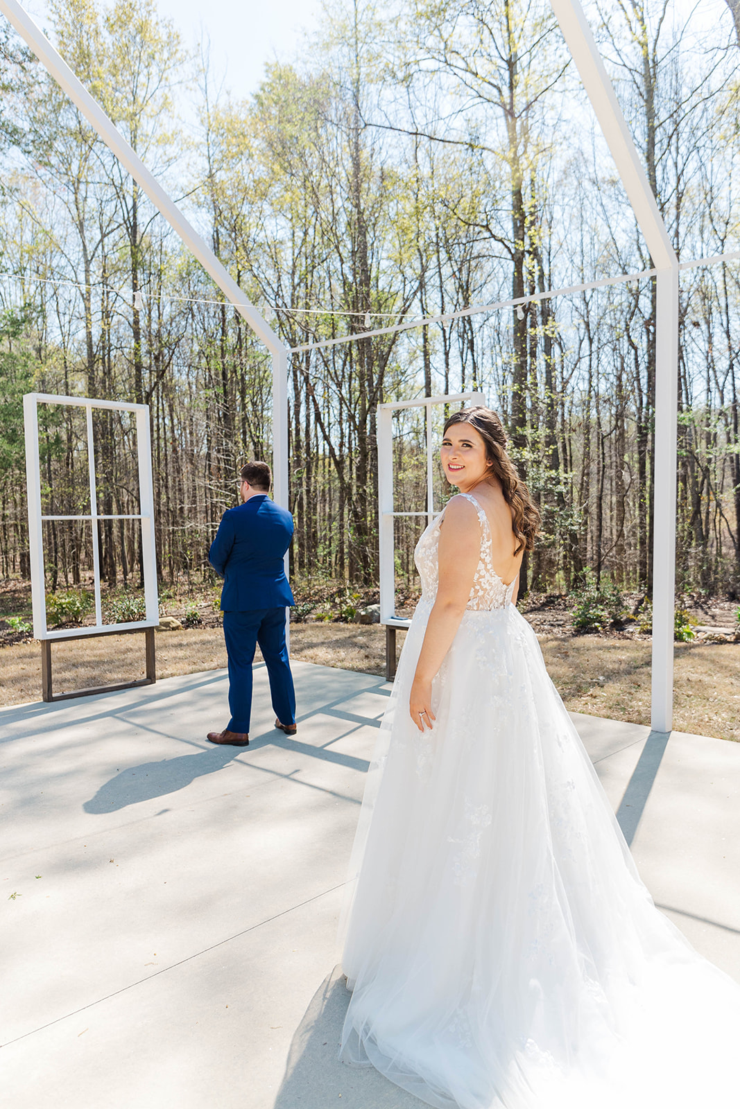 A bride smiles over her shoulder as her groom awaits their first look under the chapel frame at White Fox Cottage