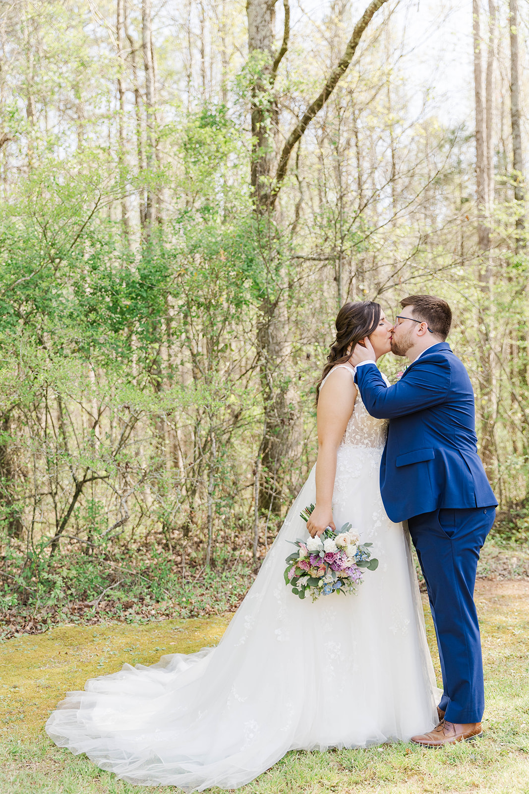 Newlyweds kiss and stand in the lawn on the forest's edge