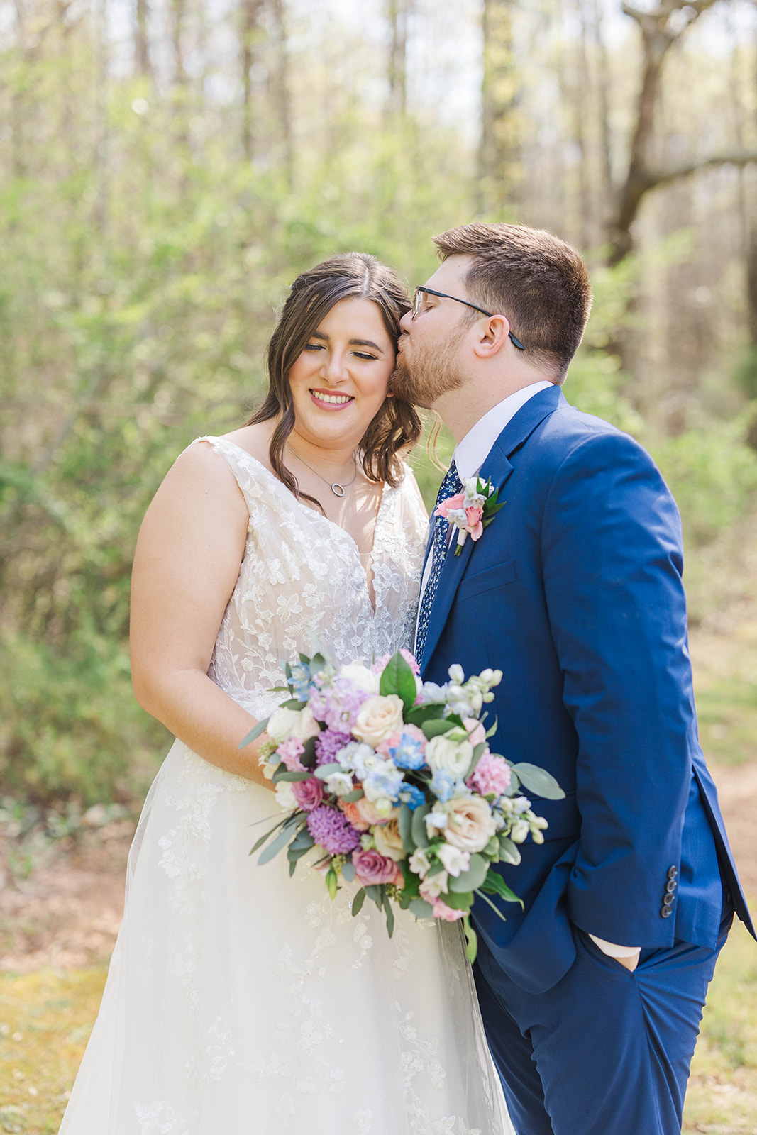 A groom in a blue suit kisses his happy bride in a lawn at White Fox Cottage