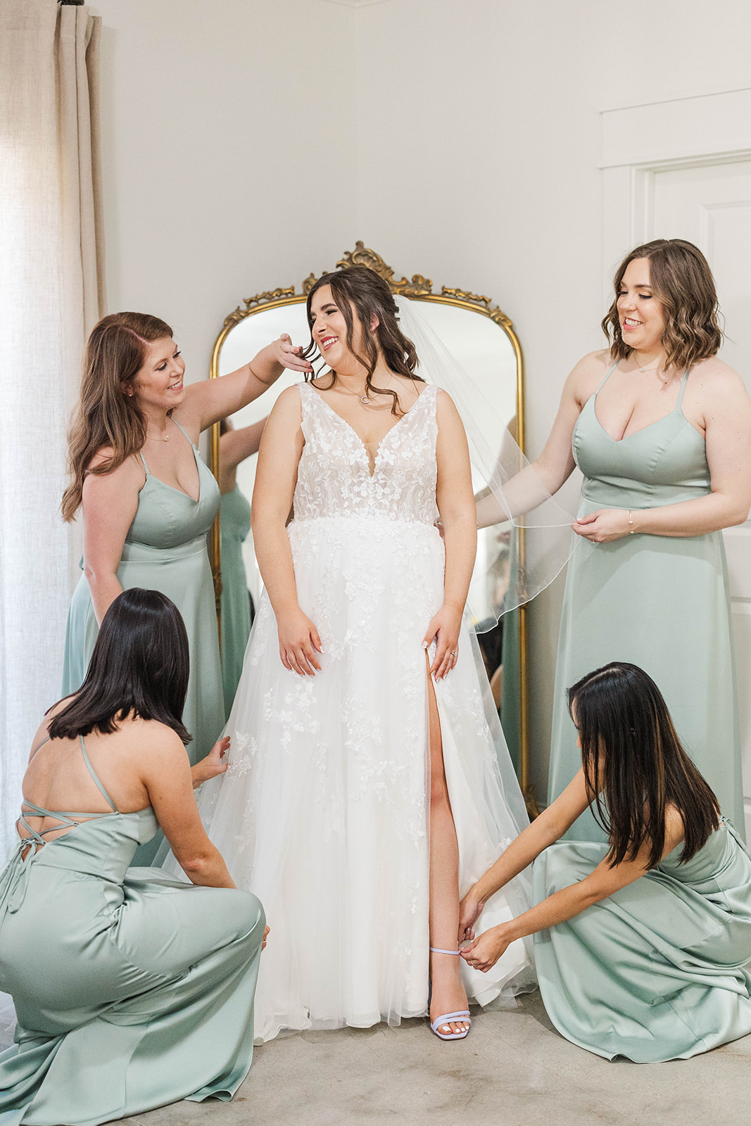 Bridesmaids in green admire the bride in her dress and help her get ready