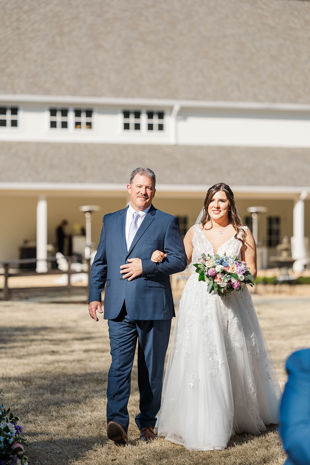 A happy dad walks his daughter down the aisle in a blue suit