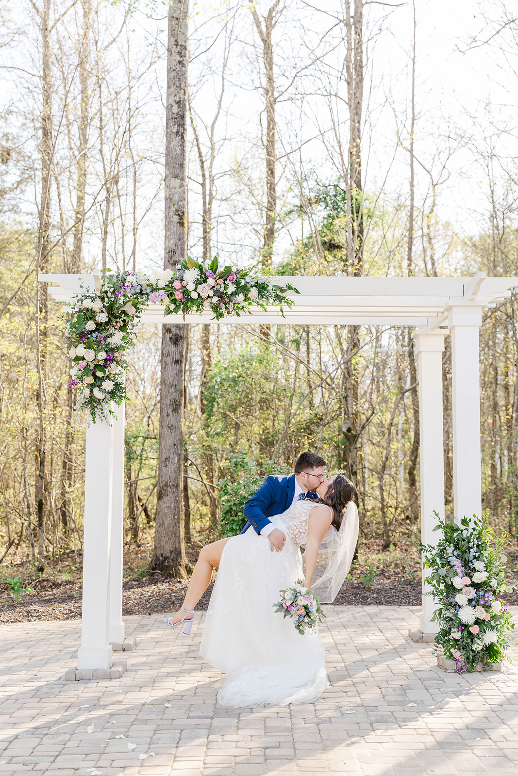 A groom kisses and dips his bride under the wedding pergola on a patio at White Fox Cottage