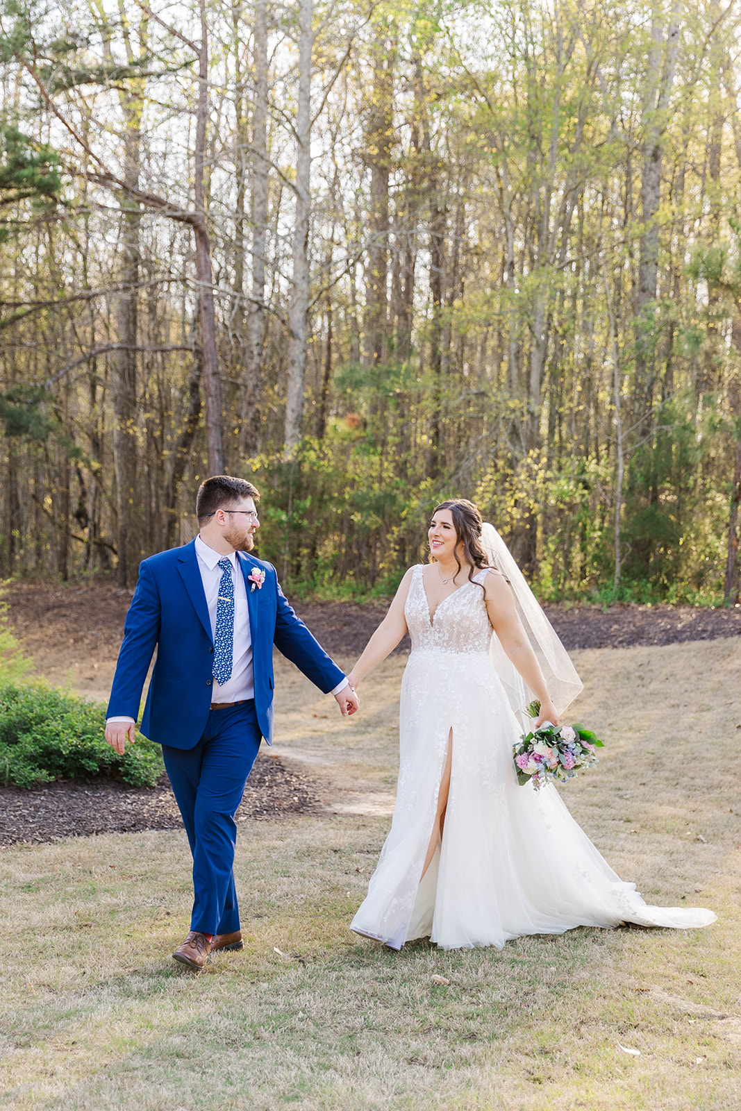 Newlyweds hold hands as the groom in blue walks his bride through the lawn