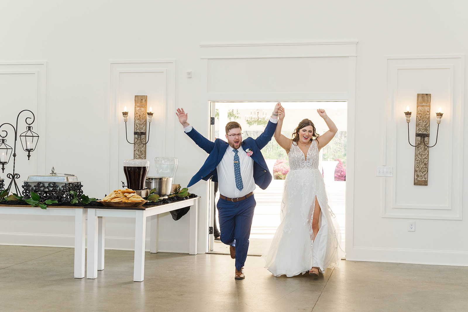 A bride and groom run into their reception with arms up