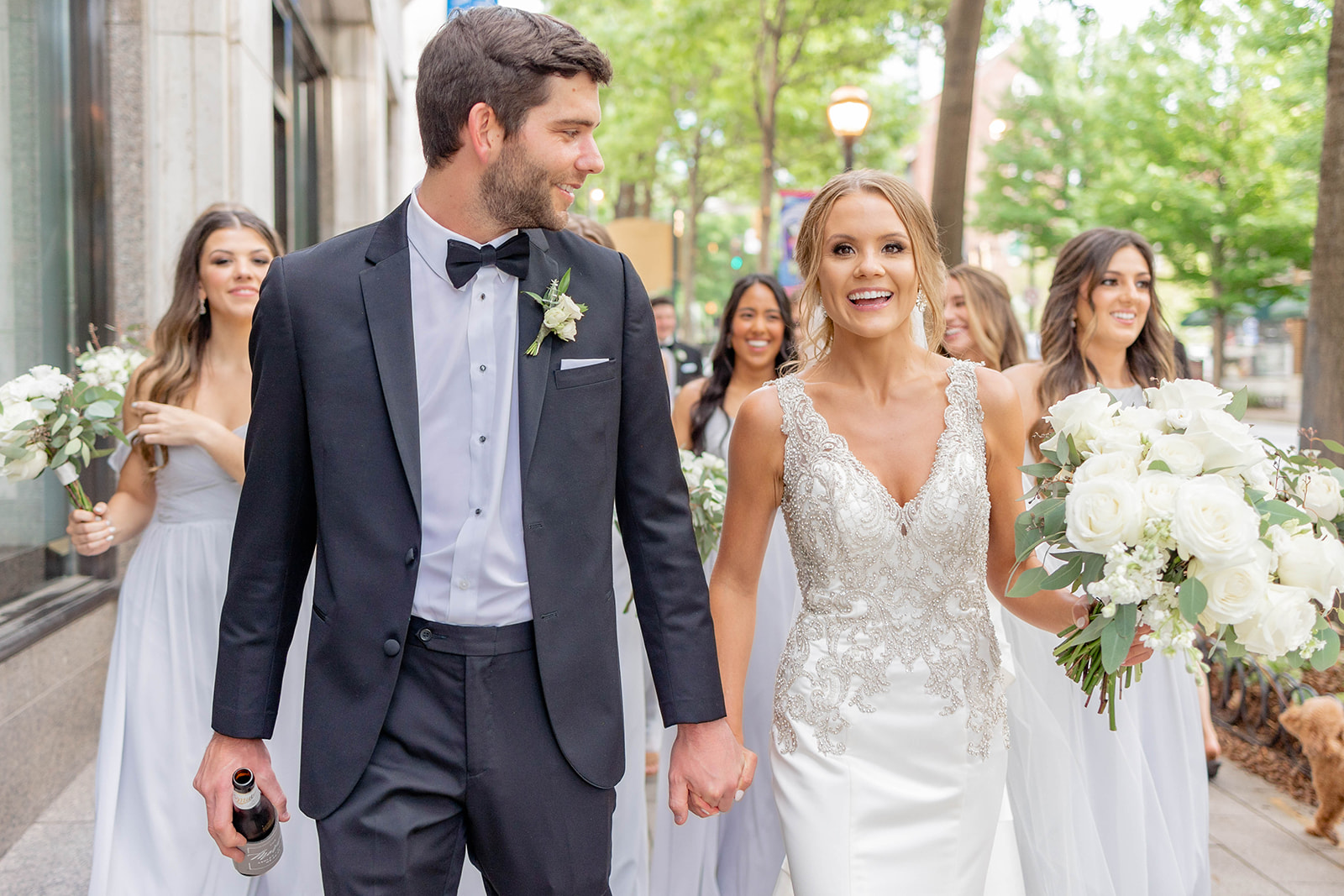 A happy bride walks with her groom holding hands and bridesmaids behind them outside one of the luxury wedding venues in Atlanta