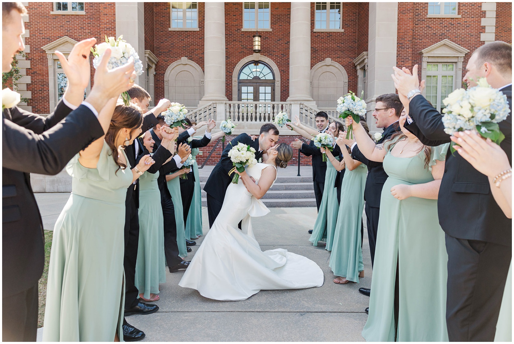 Newlyweds kiss in an aisle made by their large wedding party in black and sage during their Roswell Mill Club Wedding