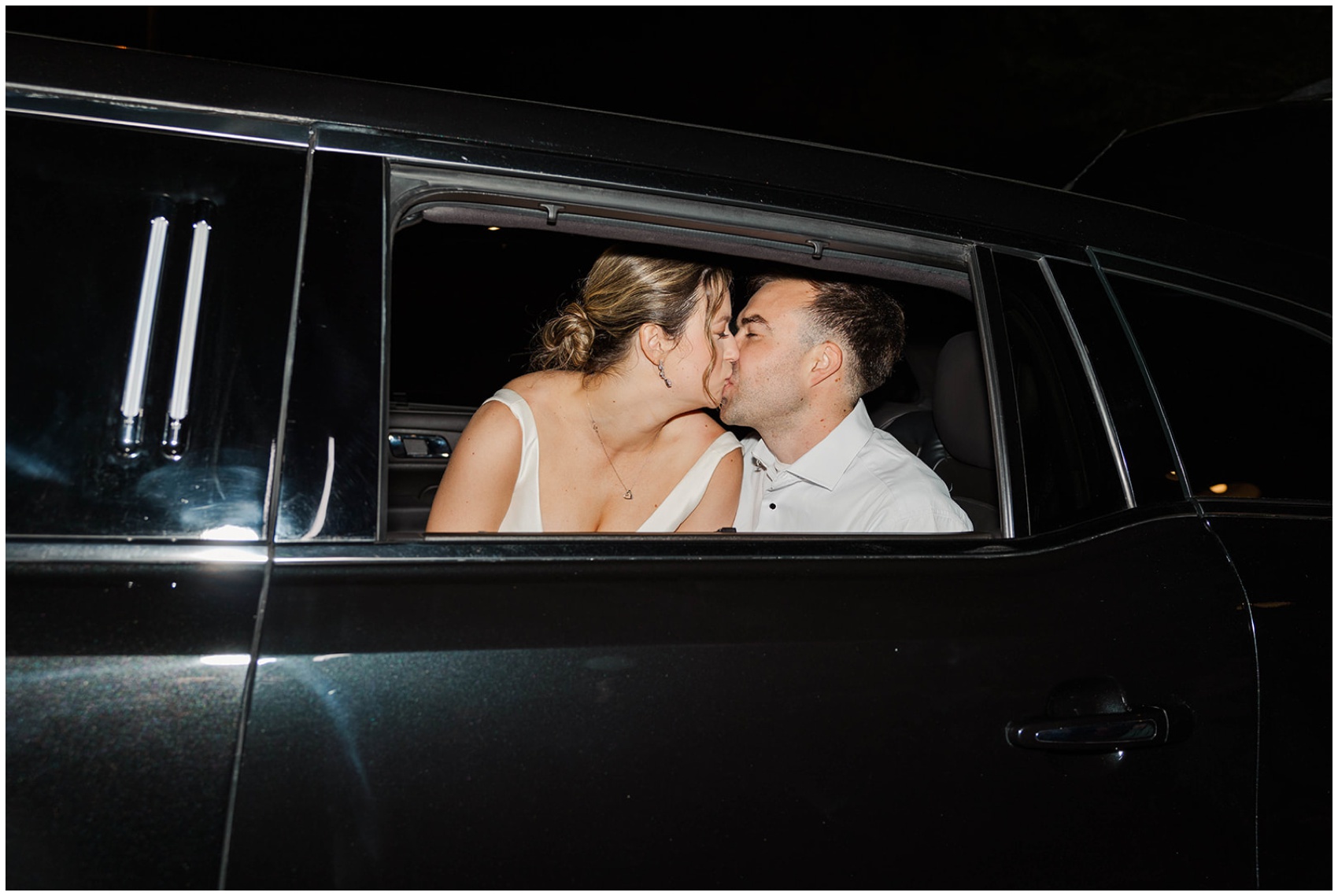 Happy newlyweds kiss in the back of a car leaving their reception