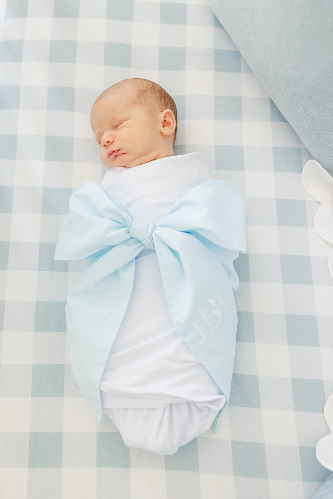 A newborn baby sleeps in a white swaddle with a blue bow around him