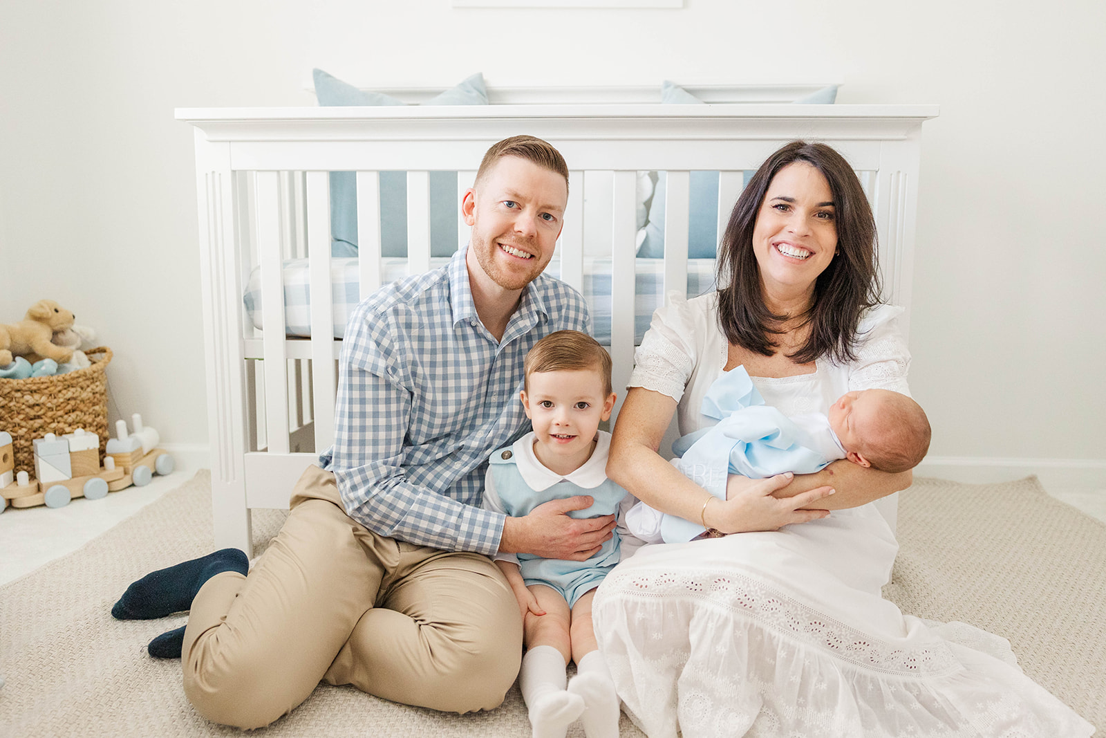 Happy mom and dad sit in the nursery holding their newborn and toddler son after using a diaper service in Atlanta