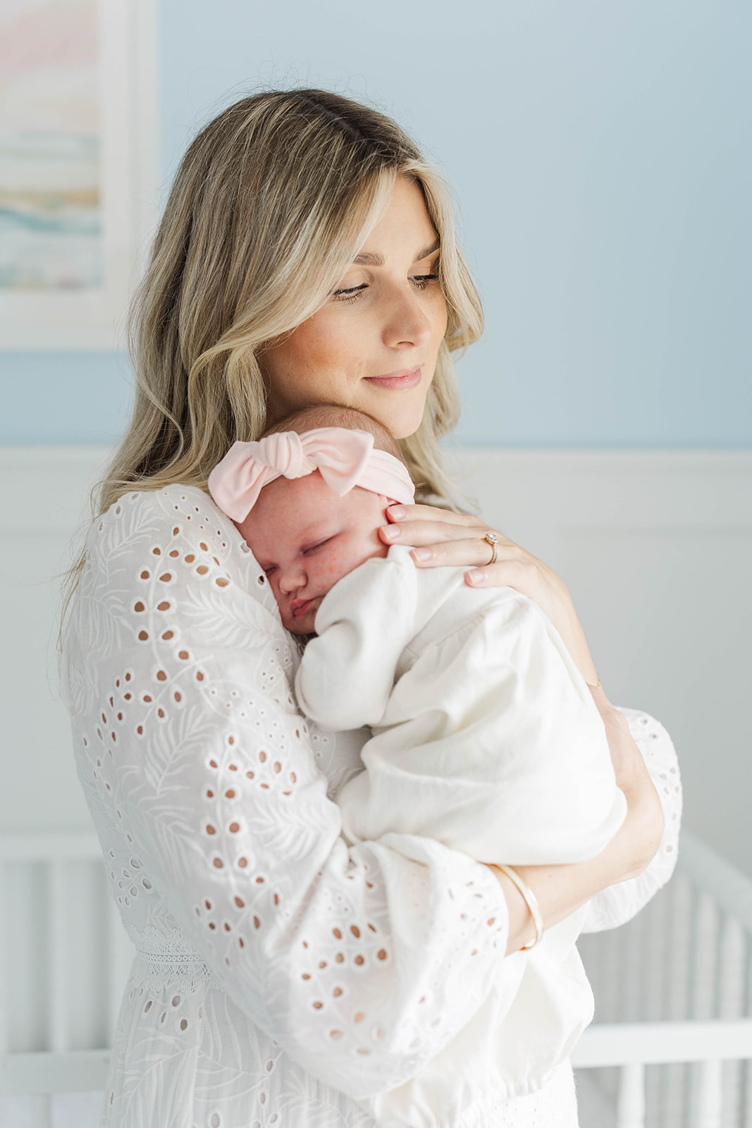 A new mom in a white dress cradles her sleeping newborn against her chest in a pink bow after meeting a lactation consultant in Atlanta