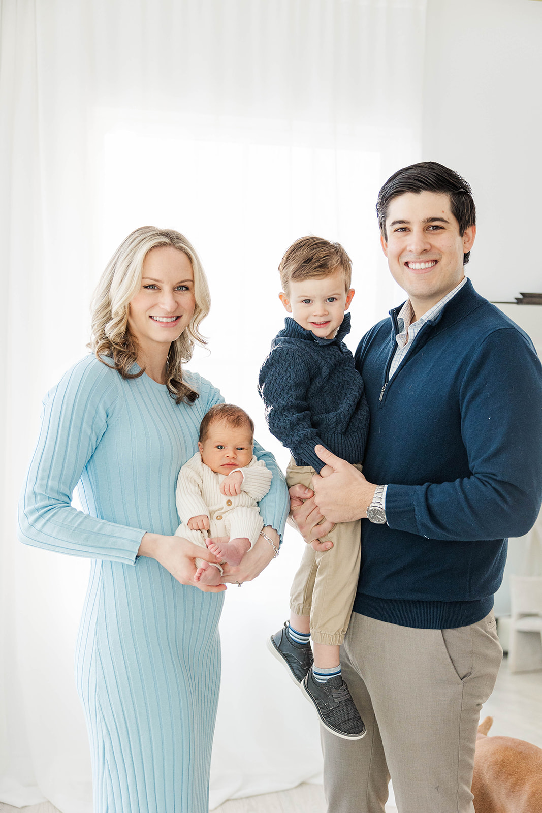 Happy mom and dad stand holding their newborn and toddler son in blue after meeting Nannies in Atlanta