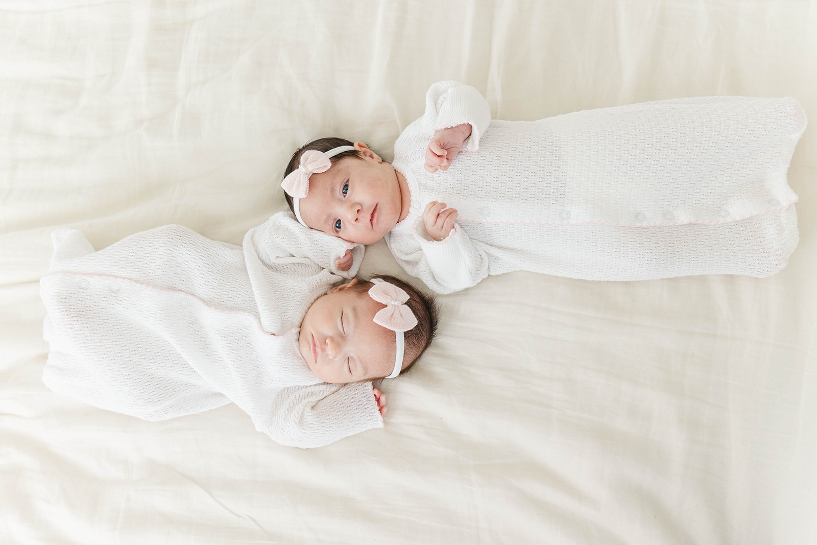 Newborn twin sisters lay on a bed head to head in white onesies after meeting a postpartum doula in Atlanta