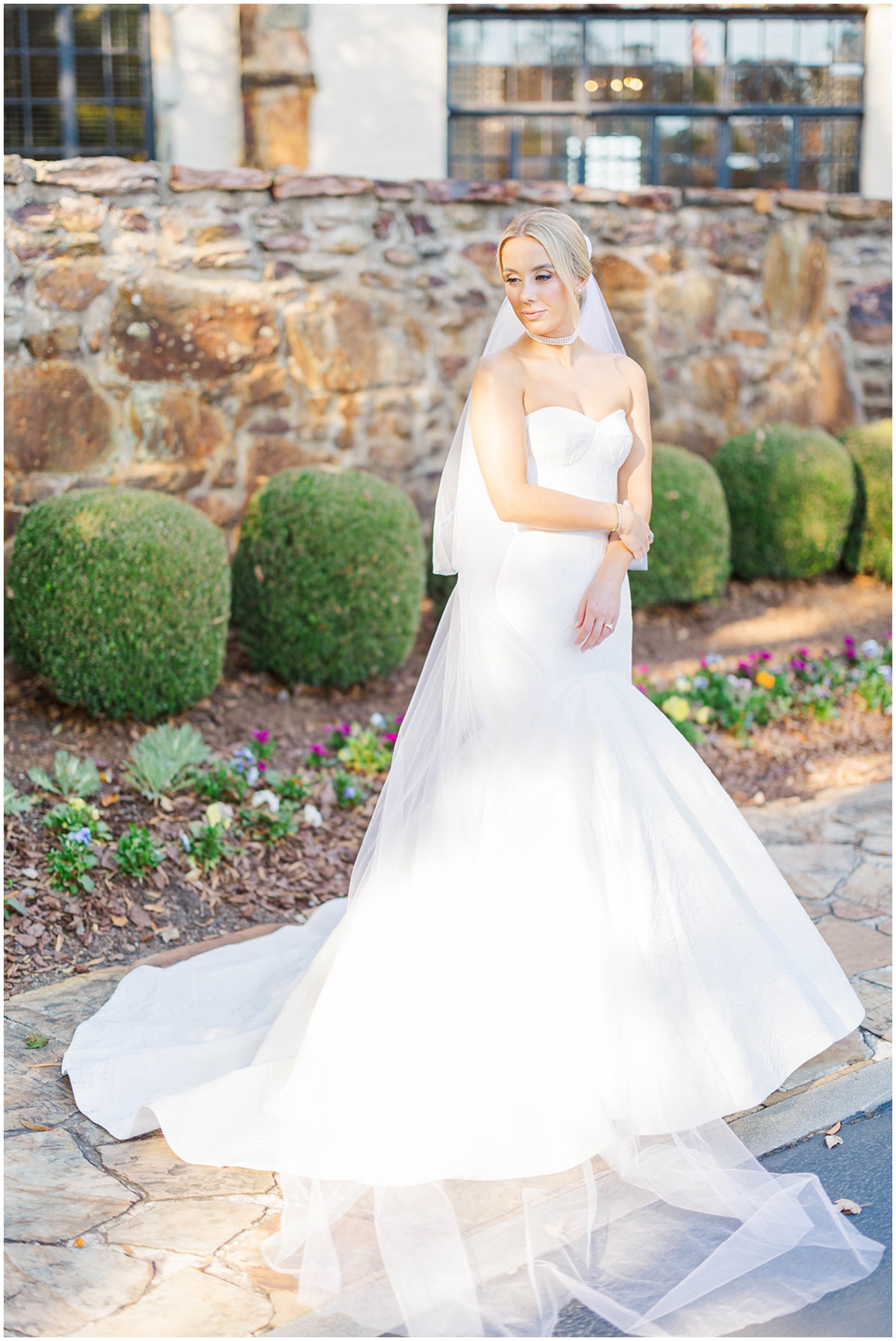 A bride smiles over her shoulder while standing in the gardens of her venue
