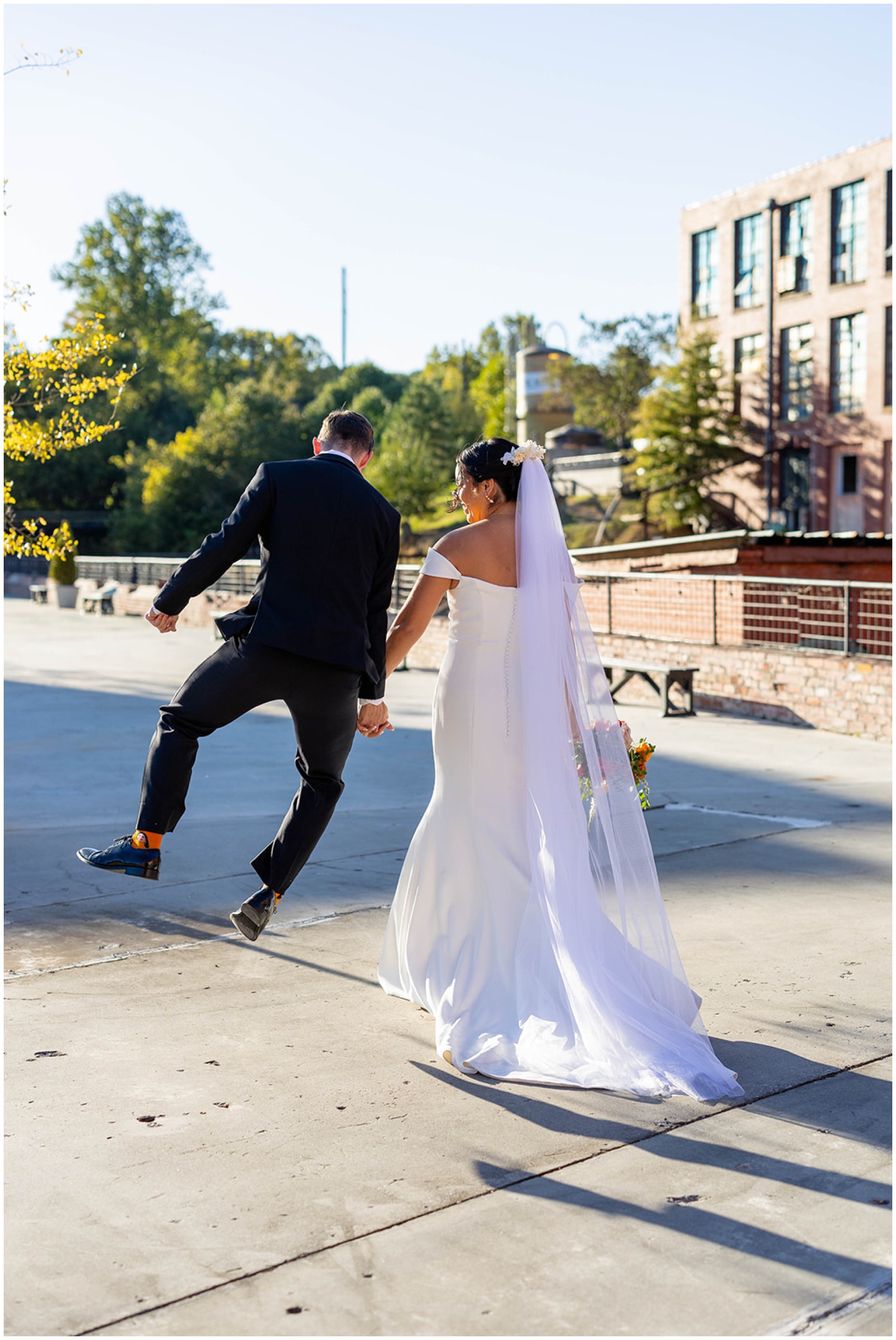A groom clicks his heels while walking with his bride on a patio