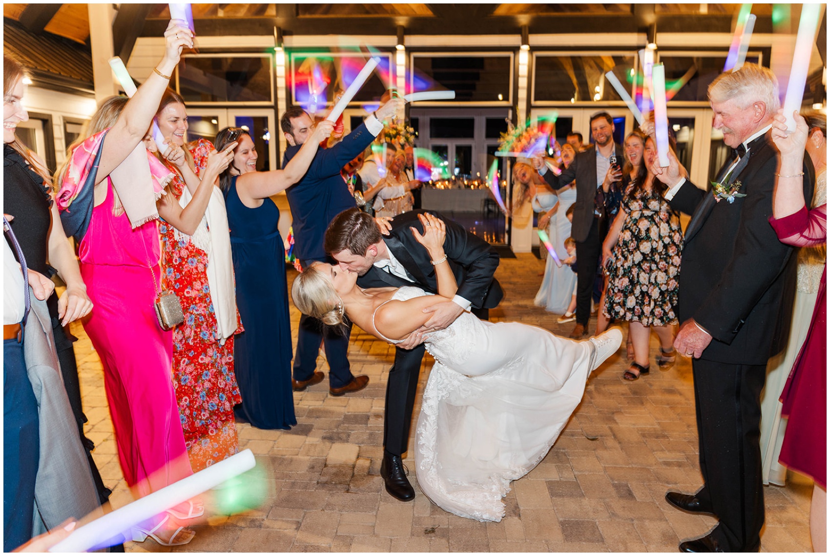 A groom dips his bride under a tunnel of led glow sticks waived by happy guests exiting their reception