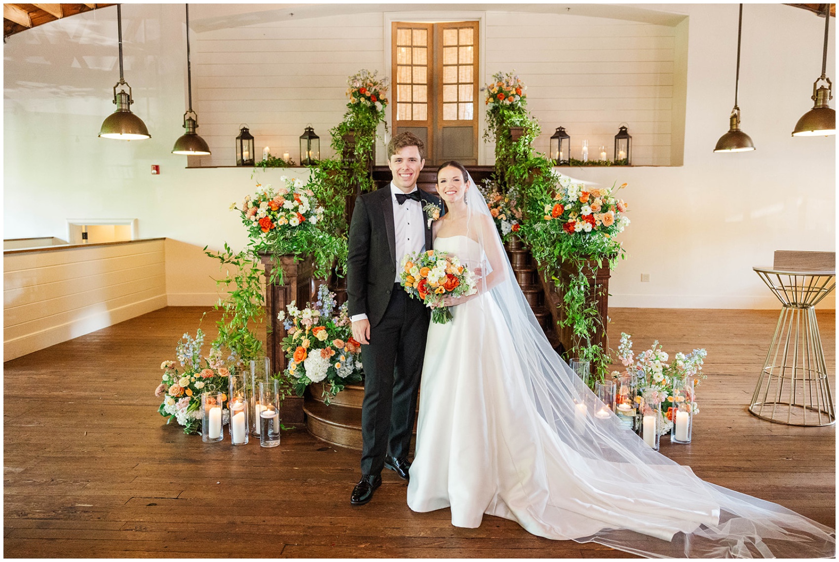 A bride and groom smile while standing at their flower covered altar