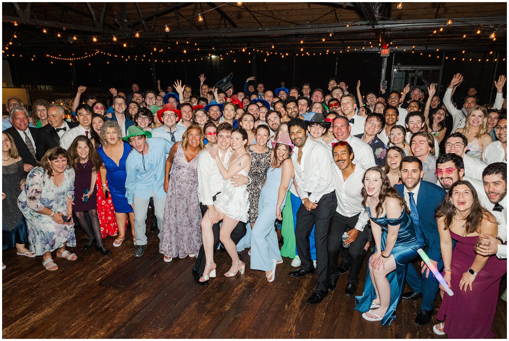 Newlyweds smile big while standing with their entire wedding in the dance floor